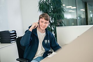 Ein Bürokaufmannlehrling sitzt am Empfang und telefoniert