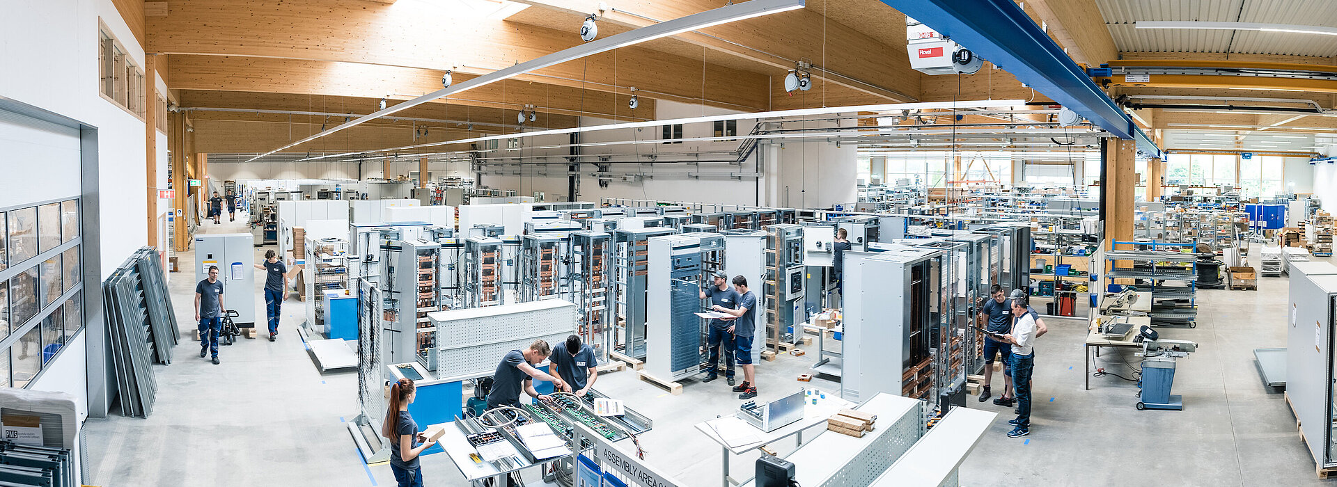 Mitarbeiter in der Schaltanlagenfertigung bei PMS in moderner Produktionshalle, umgeben von Schaltschränken und technischen Komponenten